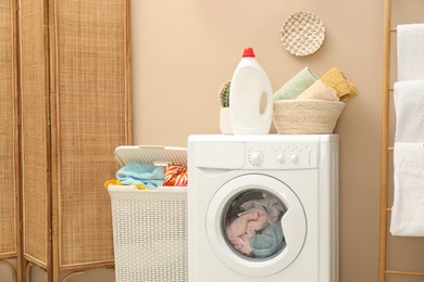 Photo of Wicker basket full of laundry, washing machine and detergent in bathroom