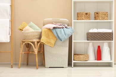 Photo of Wicker basket full of laundry and detergents in bathroom