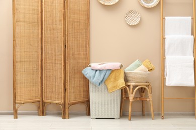 Photo of Wicker basket full of laundry and folding screen in bathroom