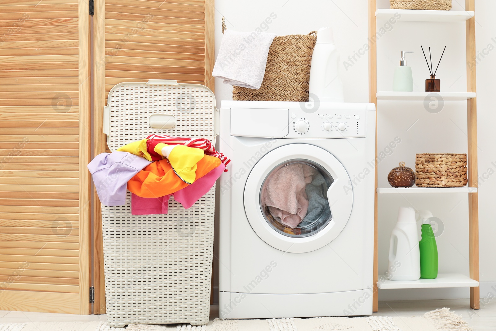 Photo of Wicker baskets with laundry, washing machine and detergents in bathroom