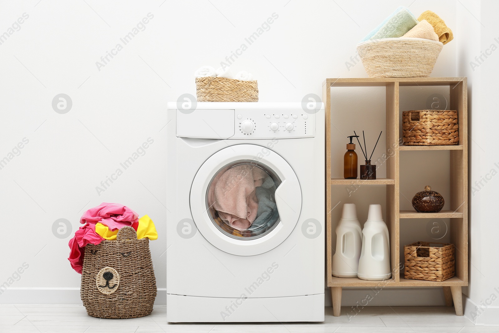 Photo of Wicker basket full of laundry, washing machine and detergents in bathroom