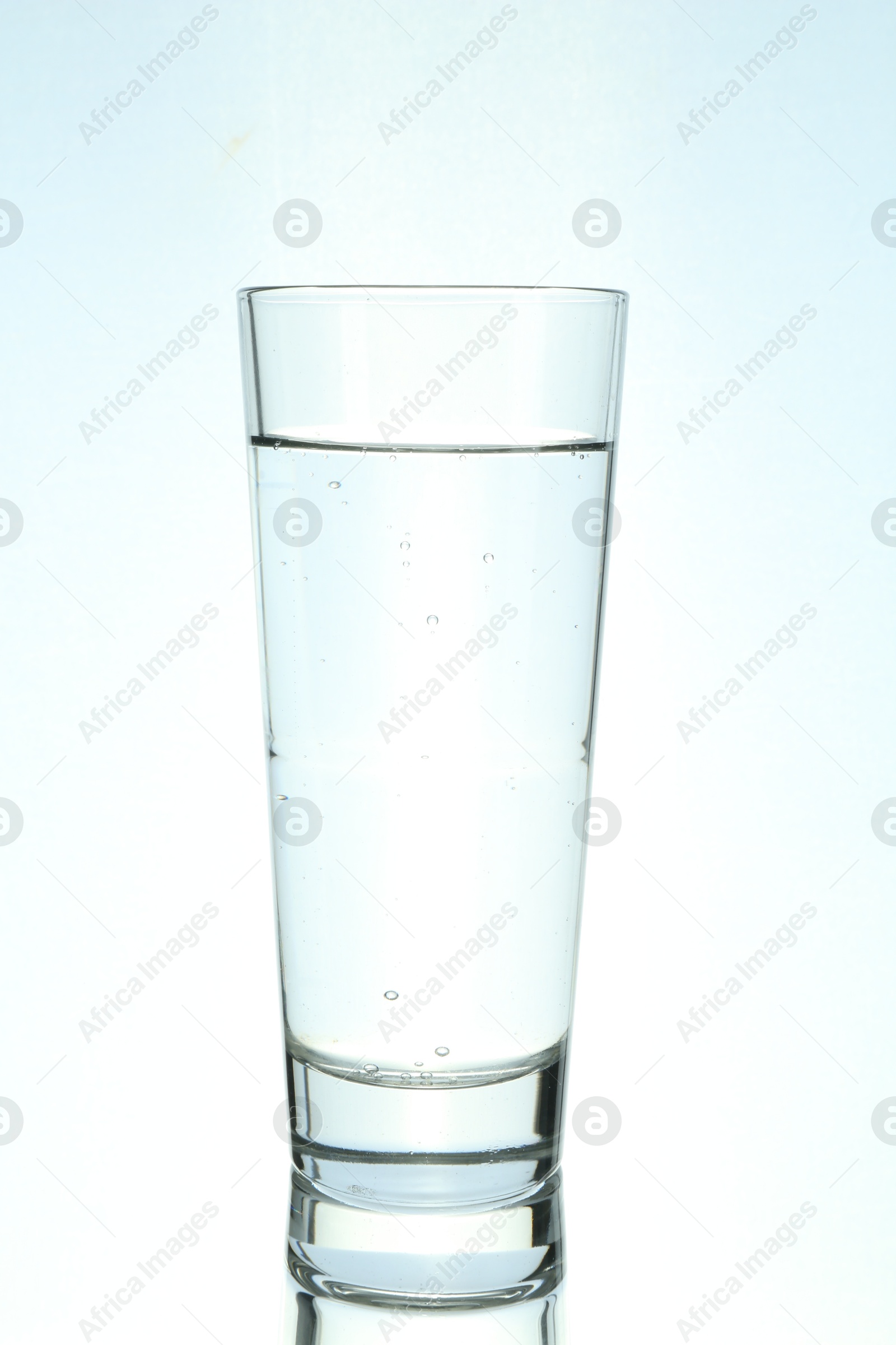 Photo of Refreshing soda water in glass on mirror surface against light background