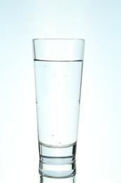 Photo of Refreshing soda water in glass on mirror surface against light background