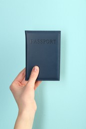 Photo of Woman holding passport in dark blue cover on turquoise background, closeup