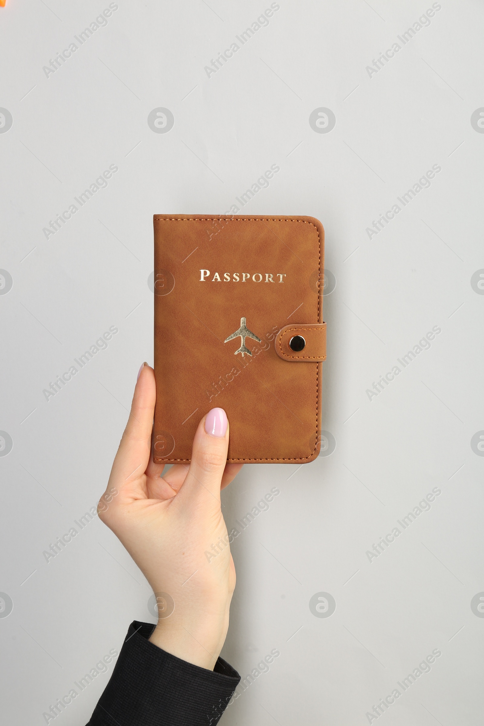 Photo of Woman holding passport in brown cover on light grey background, closeup