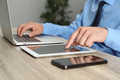 Photo of Businessman with tablet, smartphone and laptop at wooden table, closeup. Modern technology