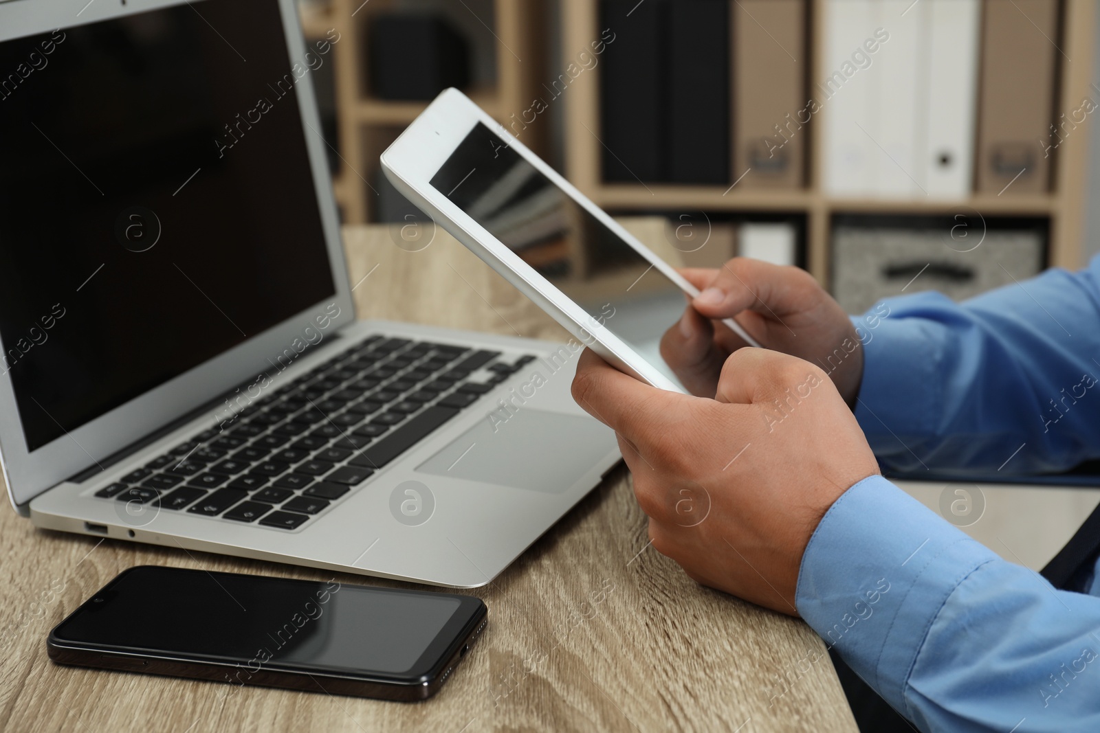 Photo of Businessman with tablet, smartphone and laptop at wooden table, closeup. Modern technology