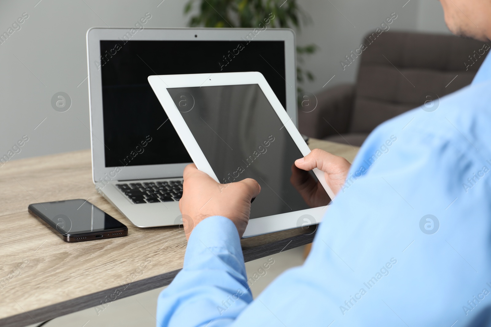 Photo of Businessman with tablet, smartphone and laptop at wooden table, closeup. Modern technology