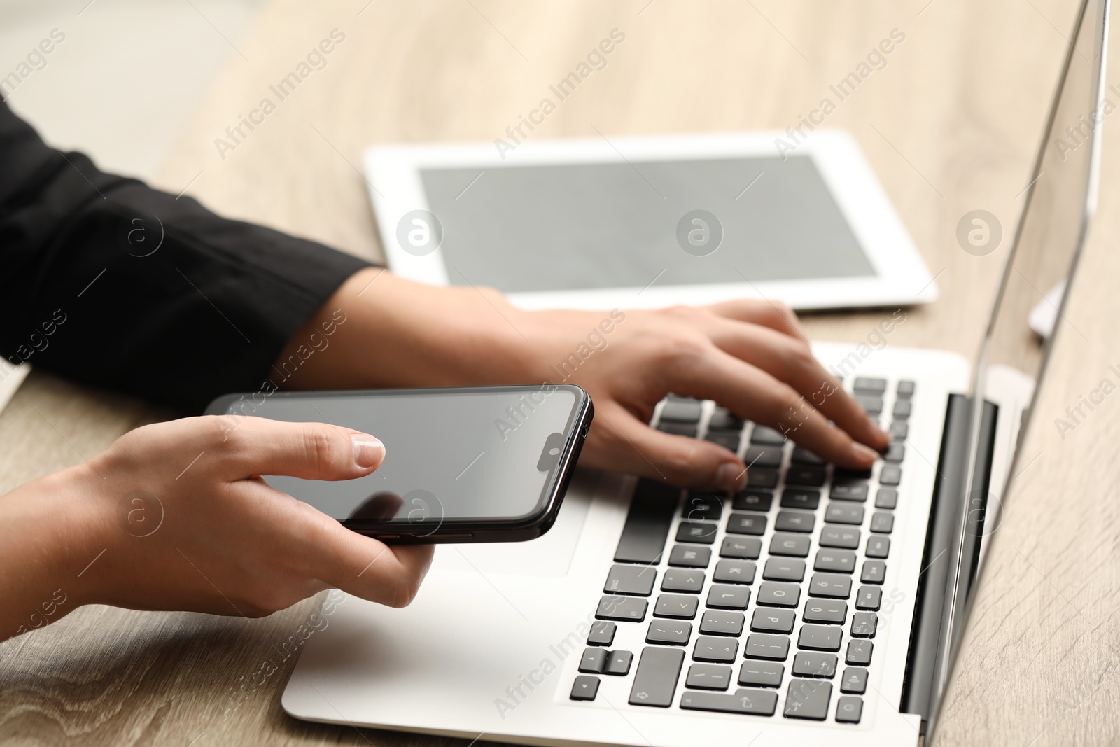 Photo of Businessman using laptop and smartphone at wooden table, closeup. Modern technology