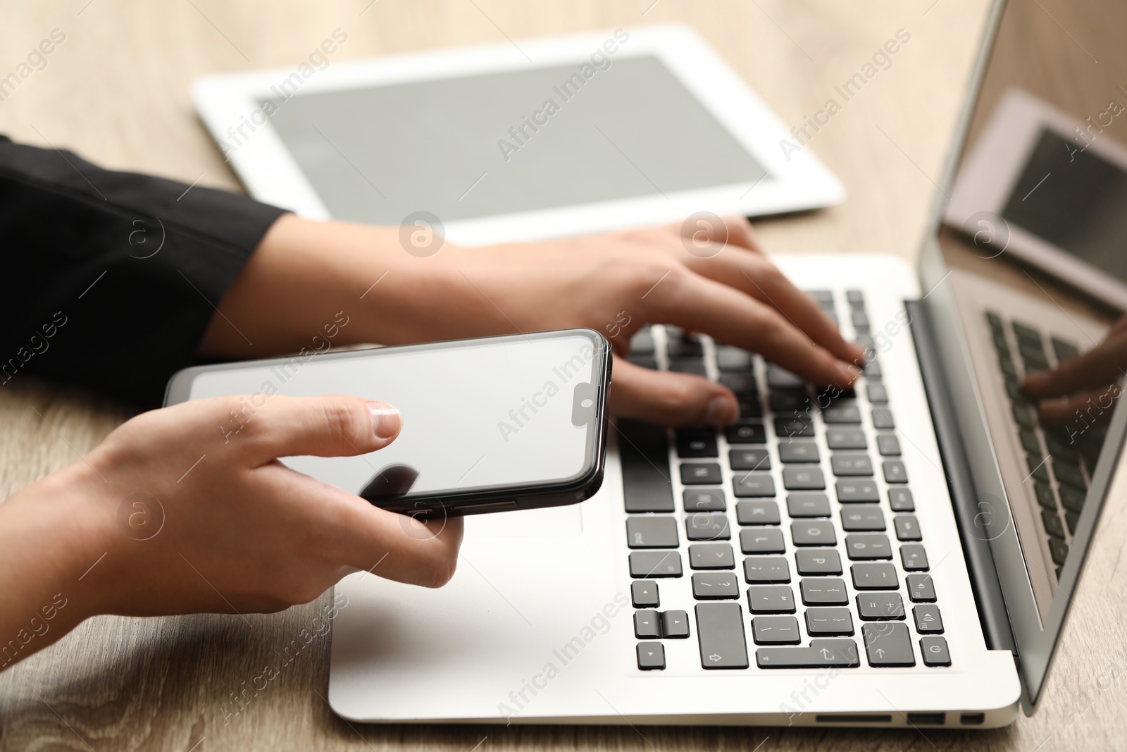 Photo of Businessman using laptop and smartphone at wooden table, closeup. Modern technology