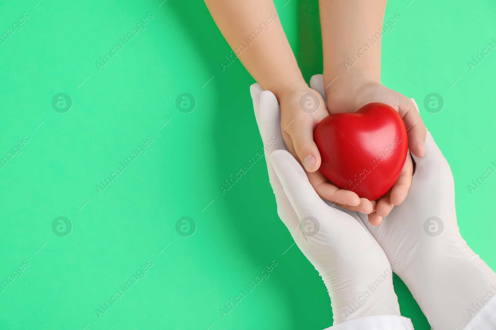 Photo of Doctor and child holding heart model on light green background, top view. Space for text