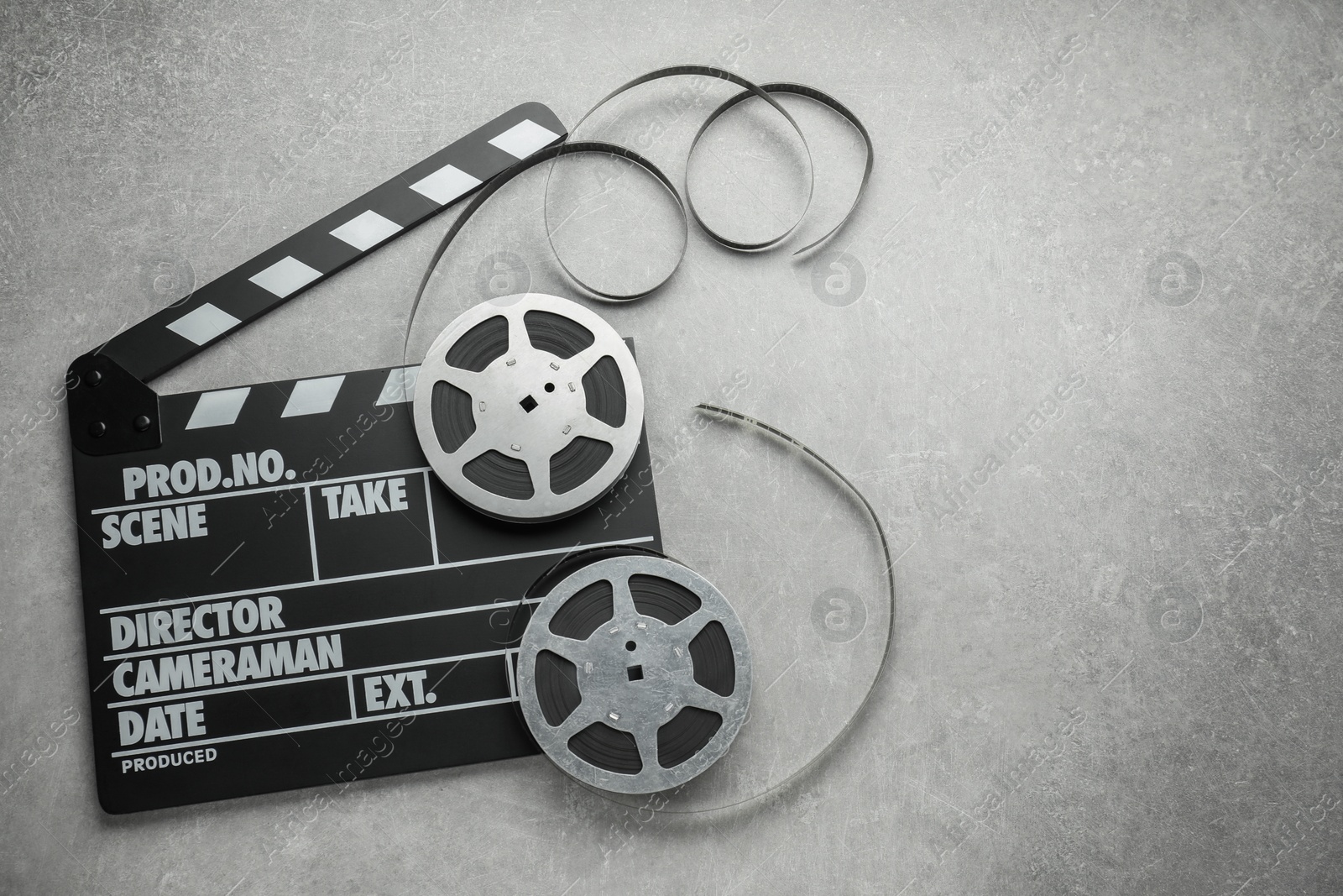 Photo of Movie clapper and film reels on grey textured table, top view. Space for text