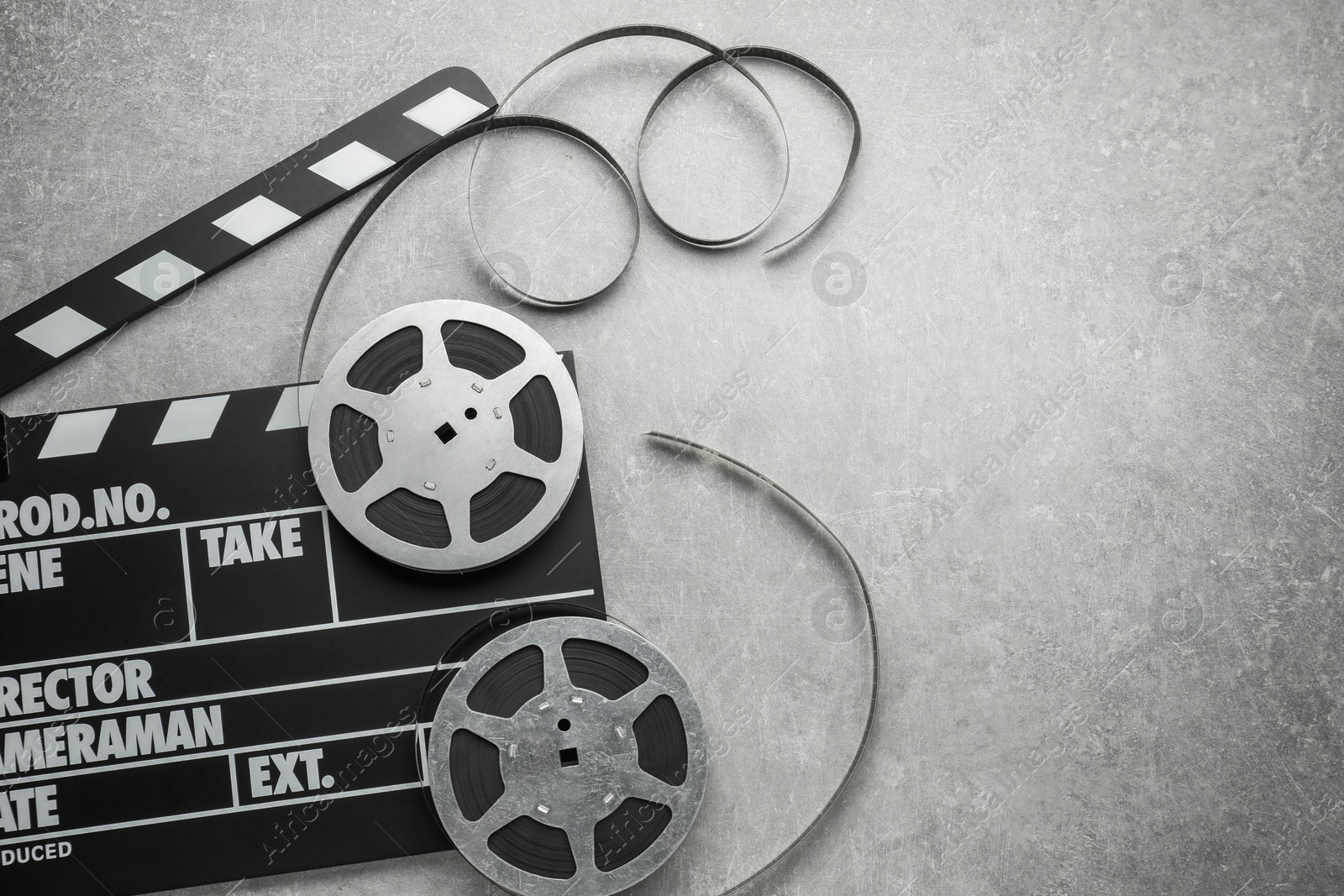 Photo of Movie clapper and film reels on grey textured table, top view. Space for text