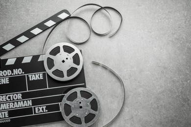 Photo of Movie clapper and film reels on grey textured table, top view. Space for text