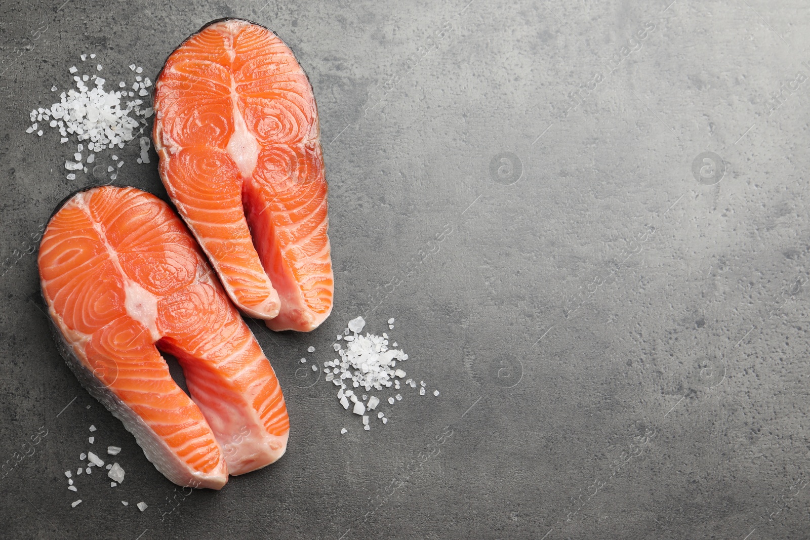 Photo of Fresh raw salmon steaks and salt on grey textured table, flat lay. Space for text