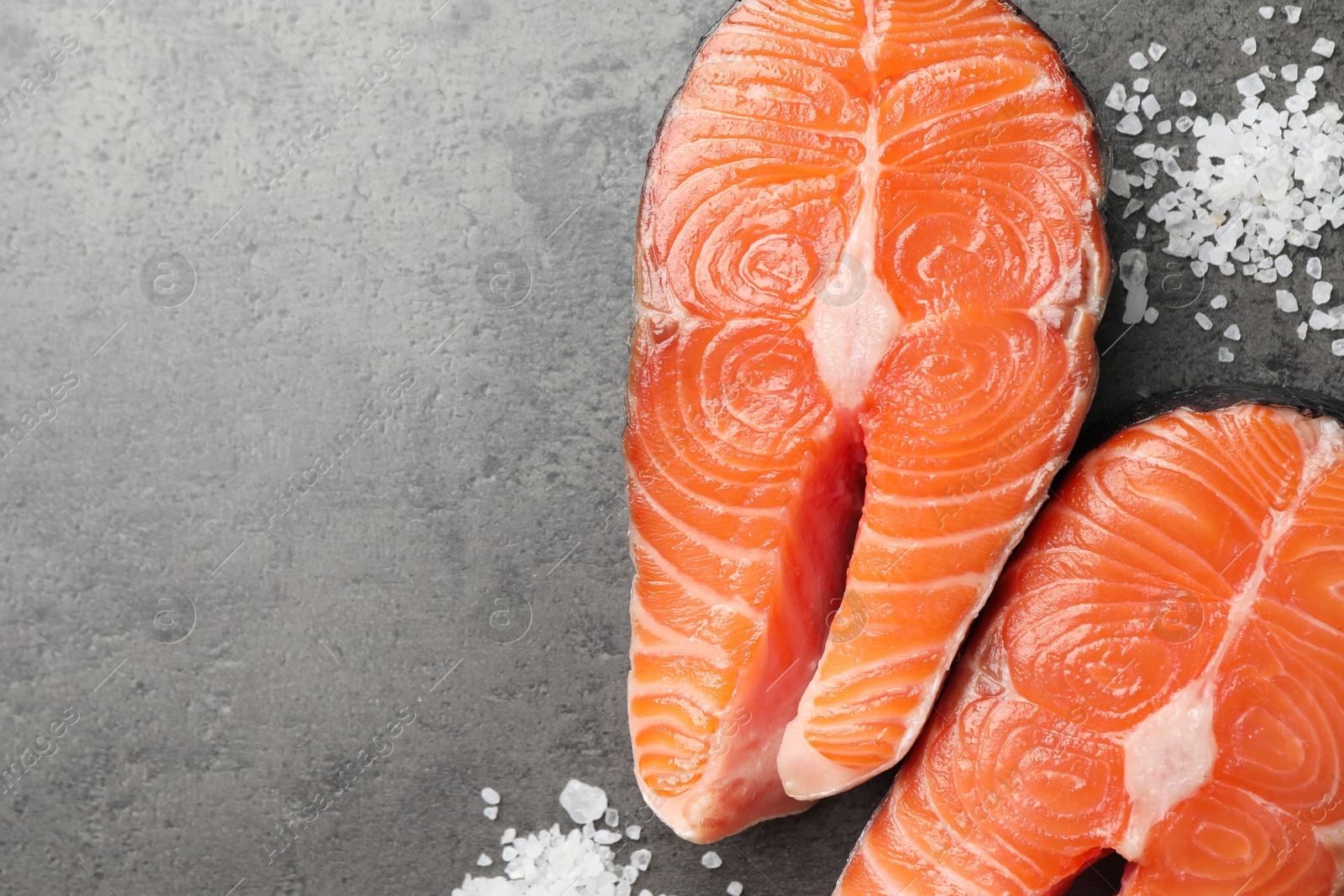 Photo of Fresh raw salmon steaks and salt on grey textured table, flat lay. Space for text