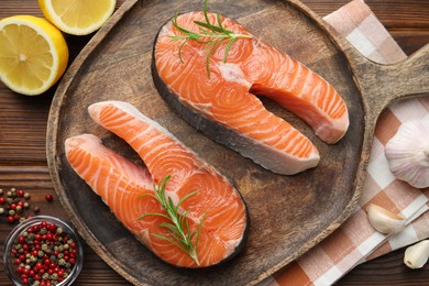 Photo of Fresh raw salmon steaks and spices on wooden table, flat lay