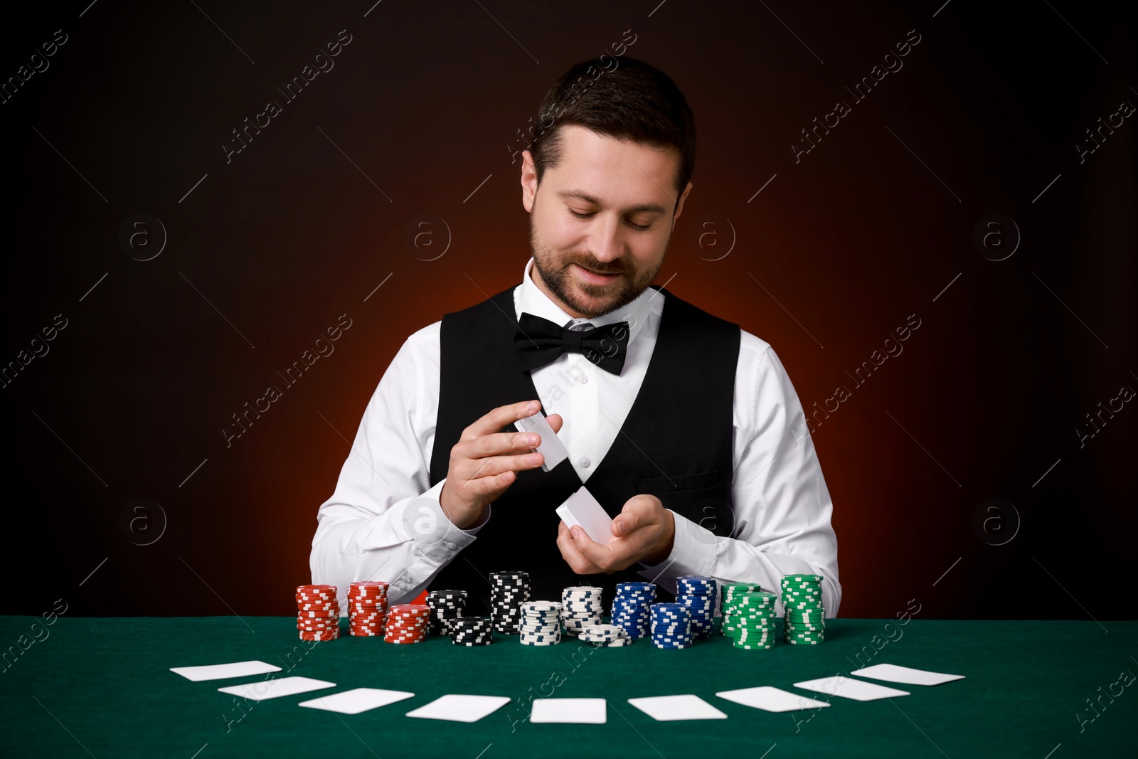 Photo of Professional croupier shuffling cards at gambling table against dark red background