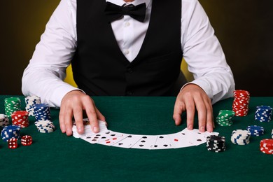 Photo of Professional croupier with playing cards at gambling table, closeup