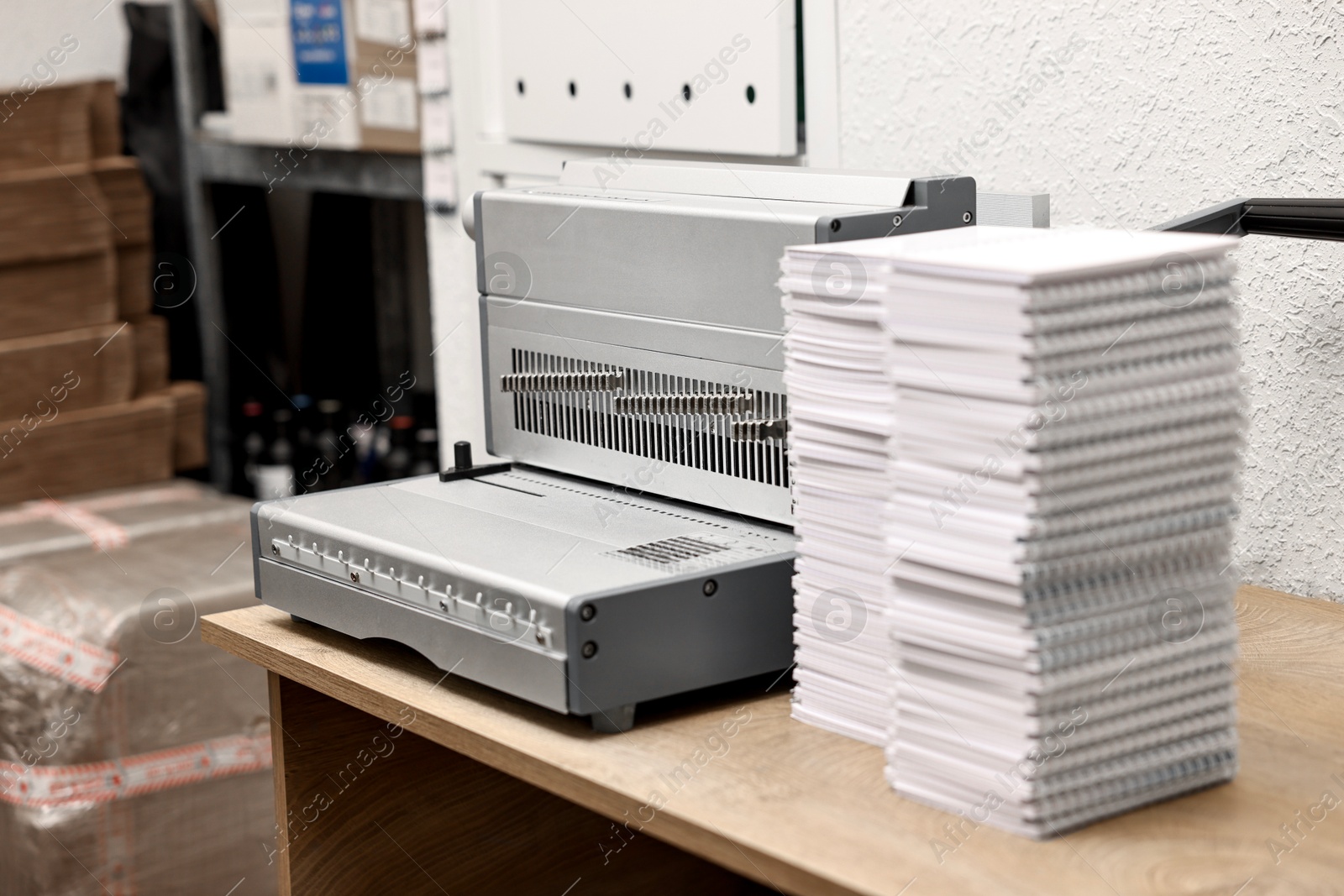 Photo of Modern binding machine and stacks of notebooks on wooden table indoors