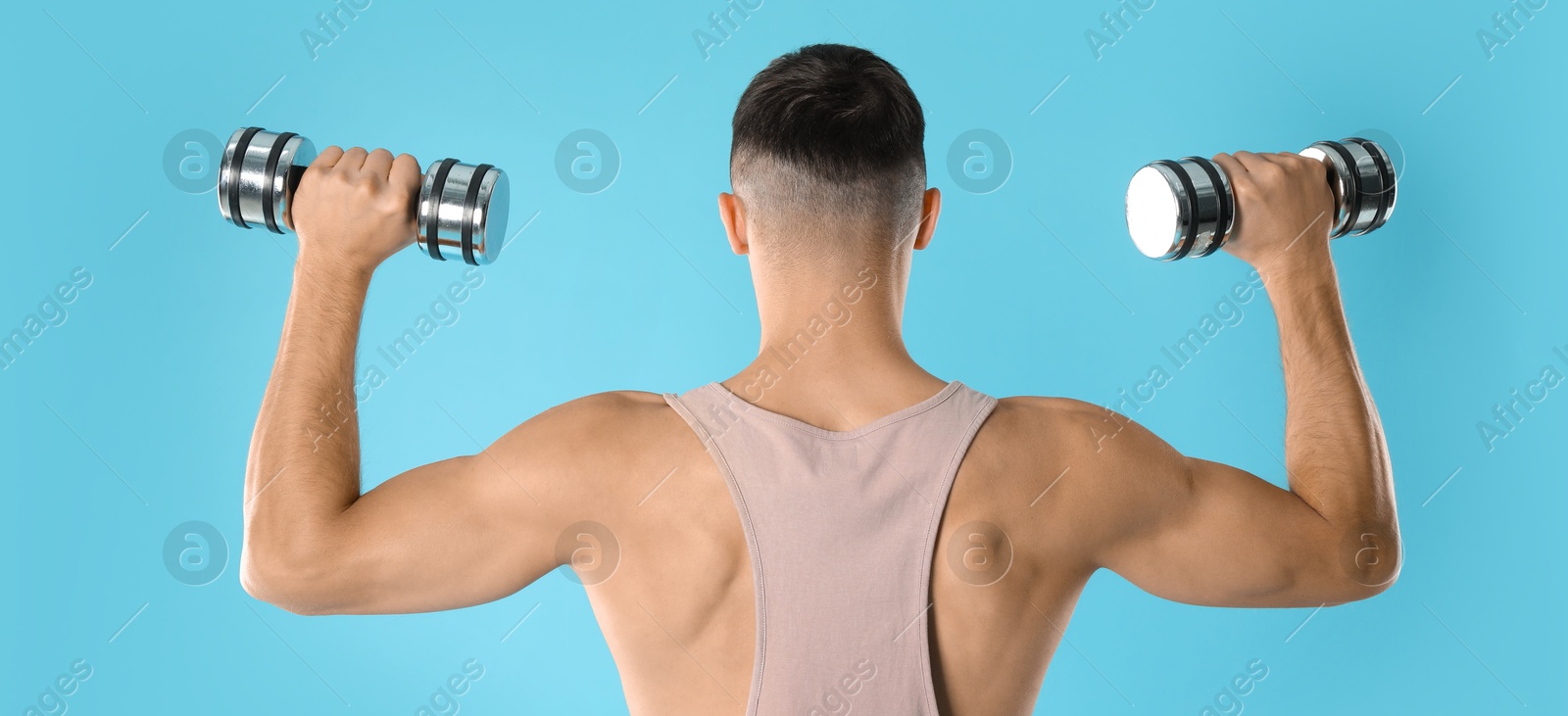 Photo of Man exercising with dumbbells on light blue background, back view