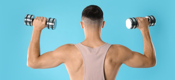 Man exercising with dumbbells on light blue background, back view