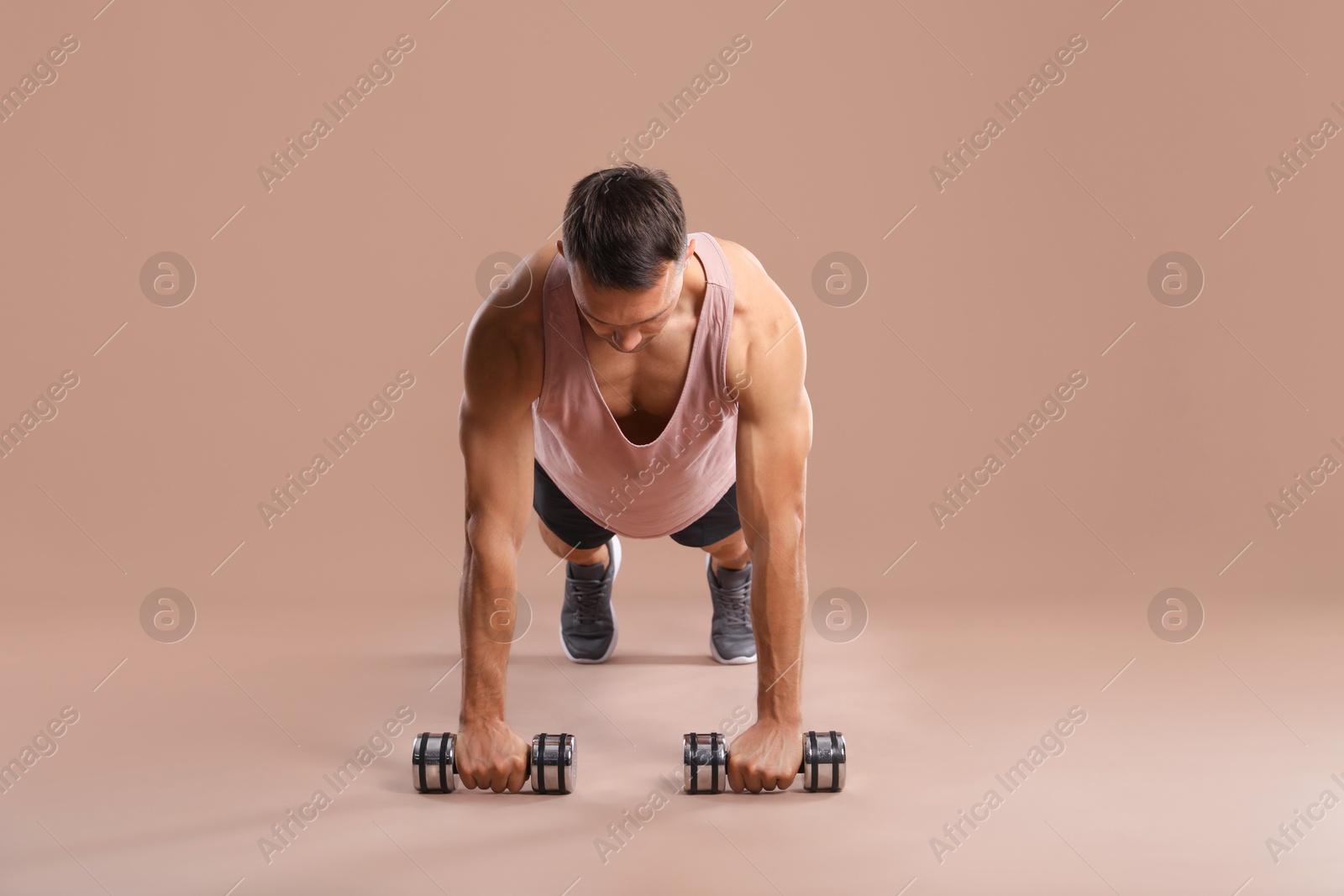 Photo of Man exercising with dumbbells on light brown background