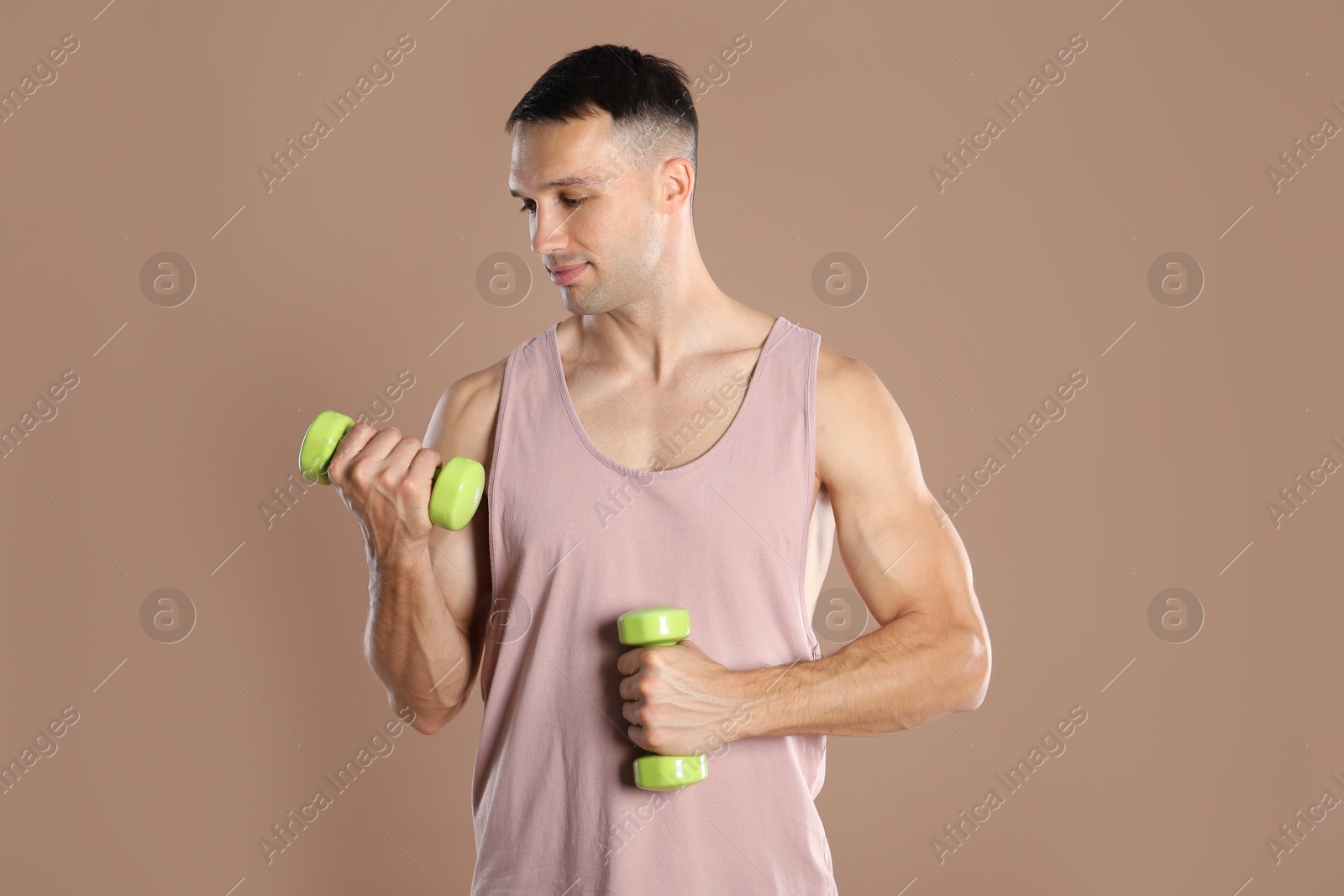 Photo of Man exercising with dumbbells on light brown background