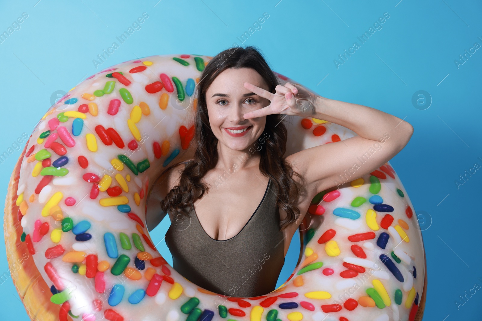 Photo of Beautiful woman in swimsuit with inflatable ring on light blue background