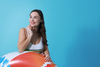 Beautiful woman in swimsuit with inflatable ring on light blue background. Space for text