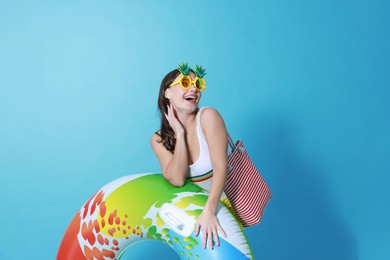 Beautiful woman wearing swimsuit and funny sunglasses with inflatable ring on light blue background