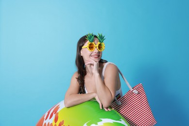 Photo of Beautiful woman wearing swimsuit and funny sunglasses with inflatable ring on light blue background