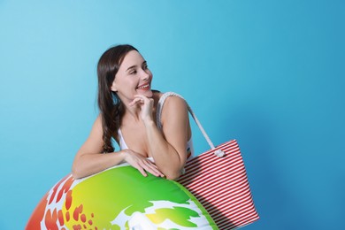 Beautiful woman in swimsuit with inflatable ring on light blue background