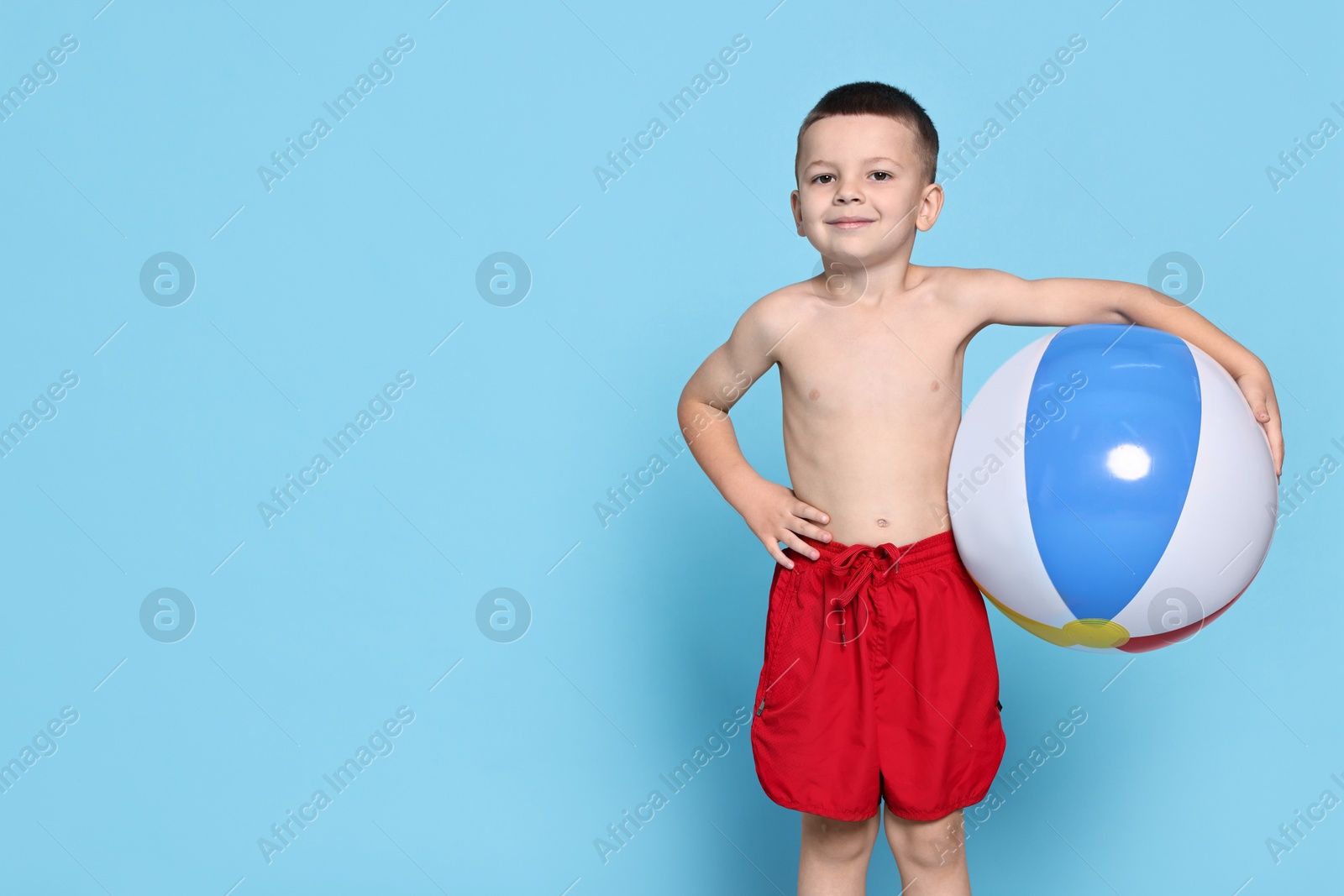 Photo of Cute little boy in beachwear with inflatable ball on light blue background. Space for text