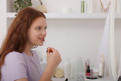 Photo of Teenage girl applying lipgloss near mirror indoors