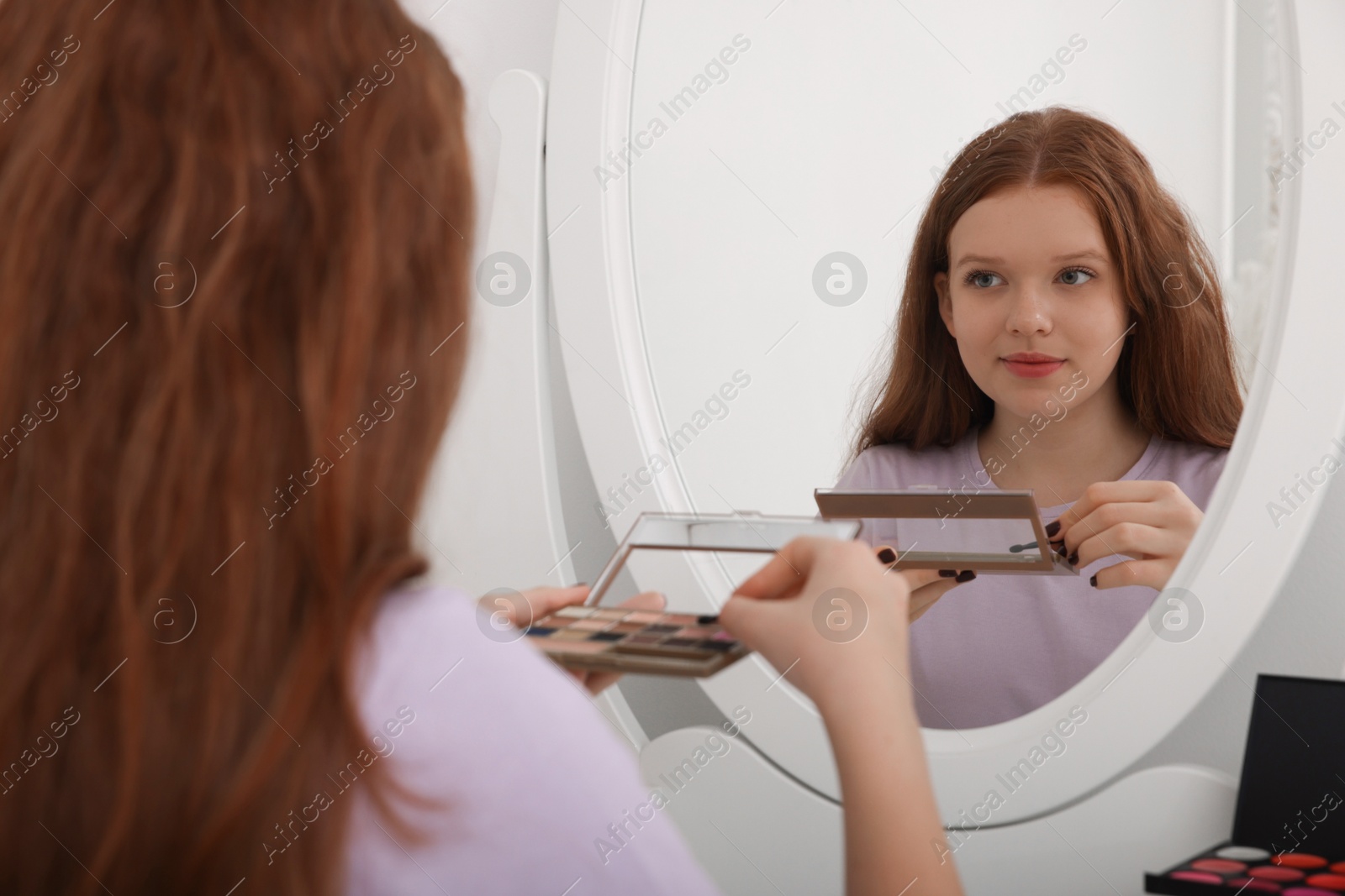 Photo of Teenage girl with eyeshadow palette near mirror indoors