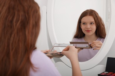 Teenage girl with eyeshadow palette near mirror indoors