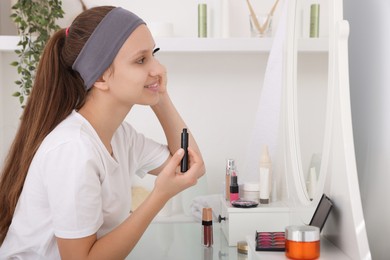 Photo of Teenage girl applying mascara near mirror indoors