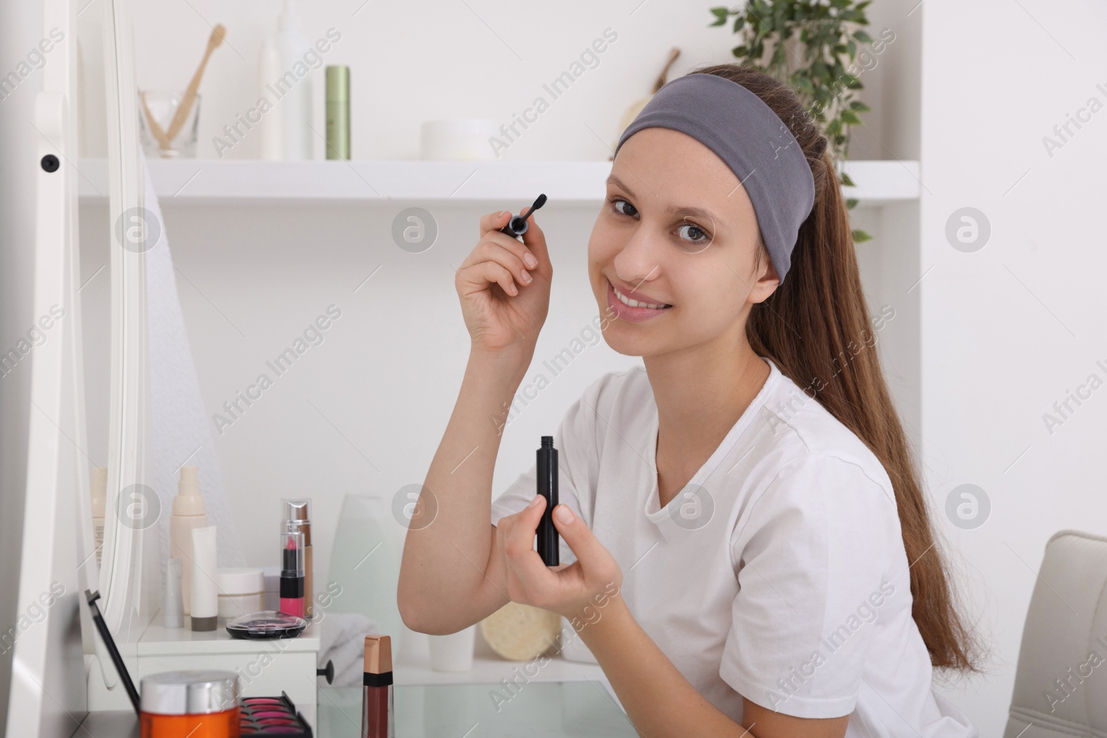 Photo of Teenage girl applying mascara near mirror indoors