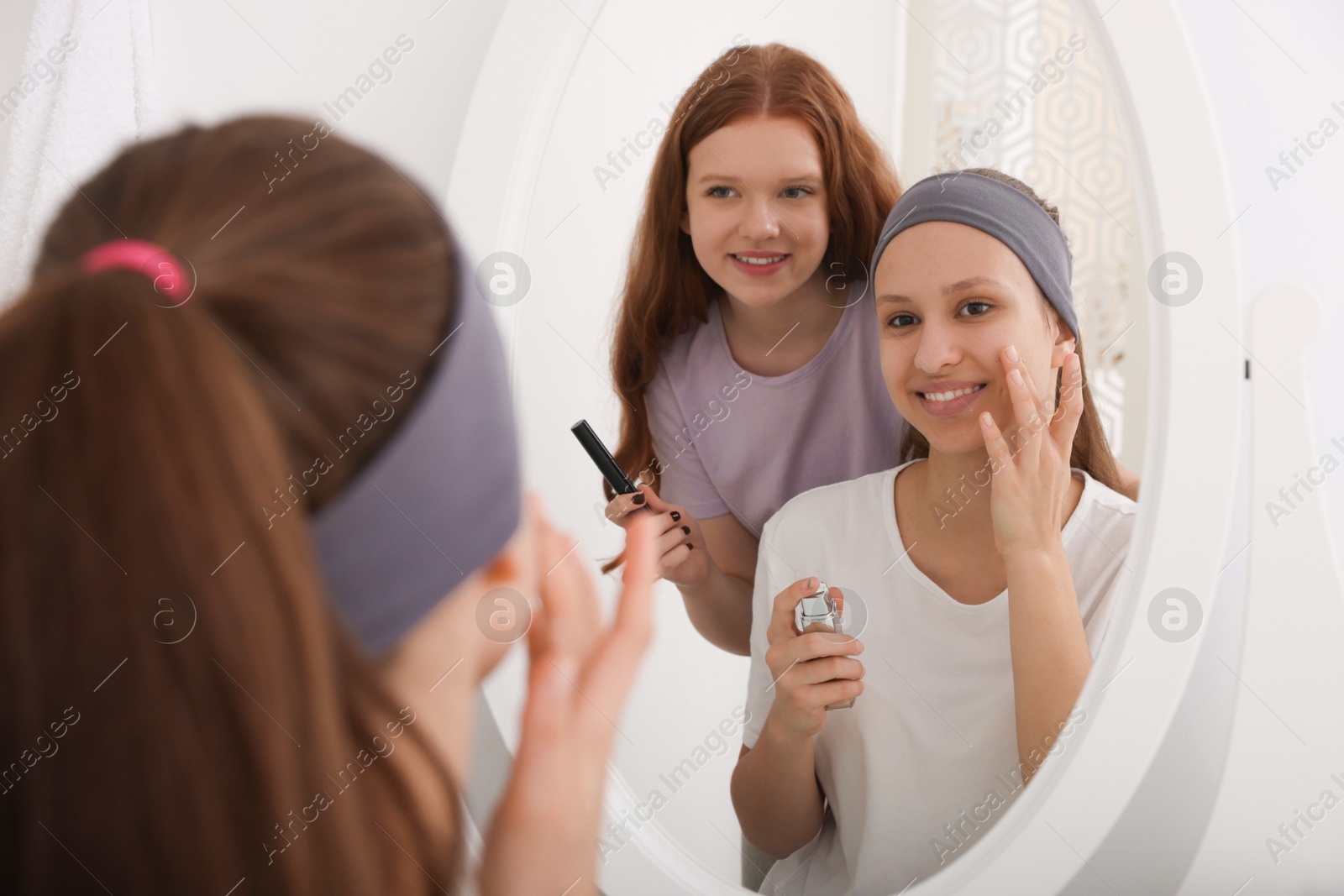 Photo of Teenage girls applying makeup products near mirror indoors