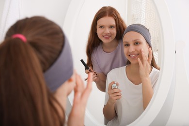 Teenage girls applying makeup products near mirror indoors