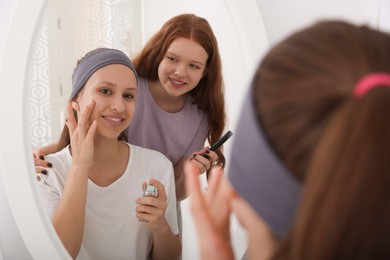 Teenage girls applying makeup products near mirror indoors