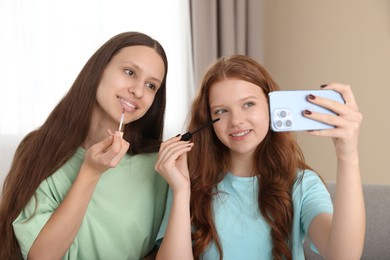 Teenage girls applying makeup products and taking selfie indoors