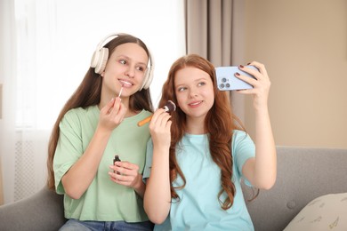 Teenage girls applying makeup products and taking selfie indoors