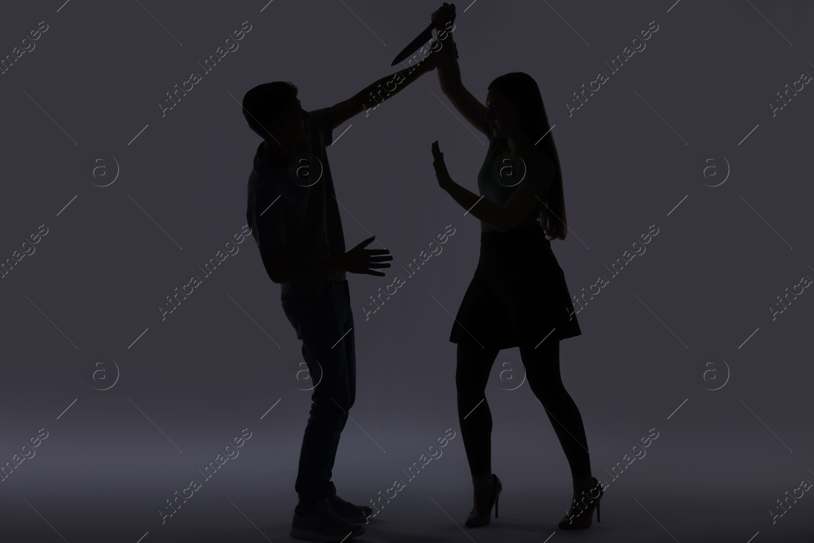 Photo of Domestic violence. Silhouette of woman with knife trying to kill her husband on grey background