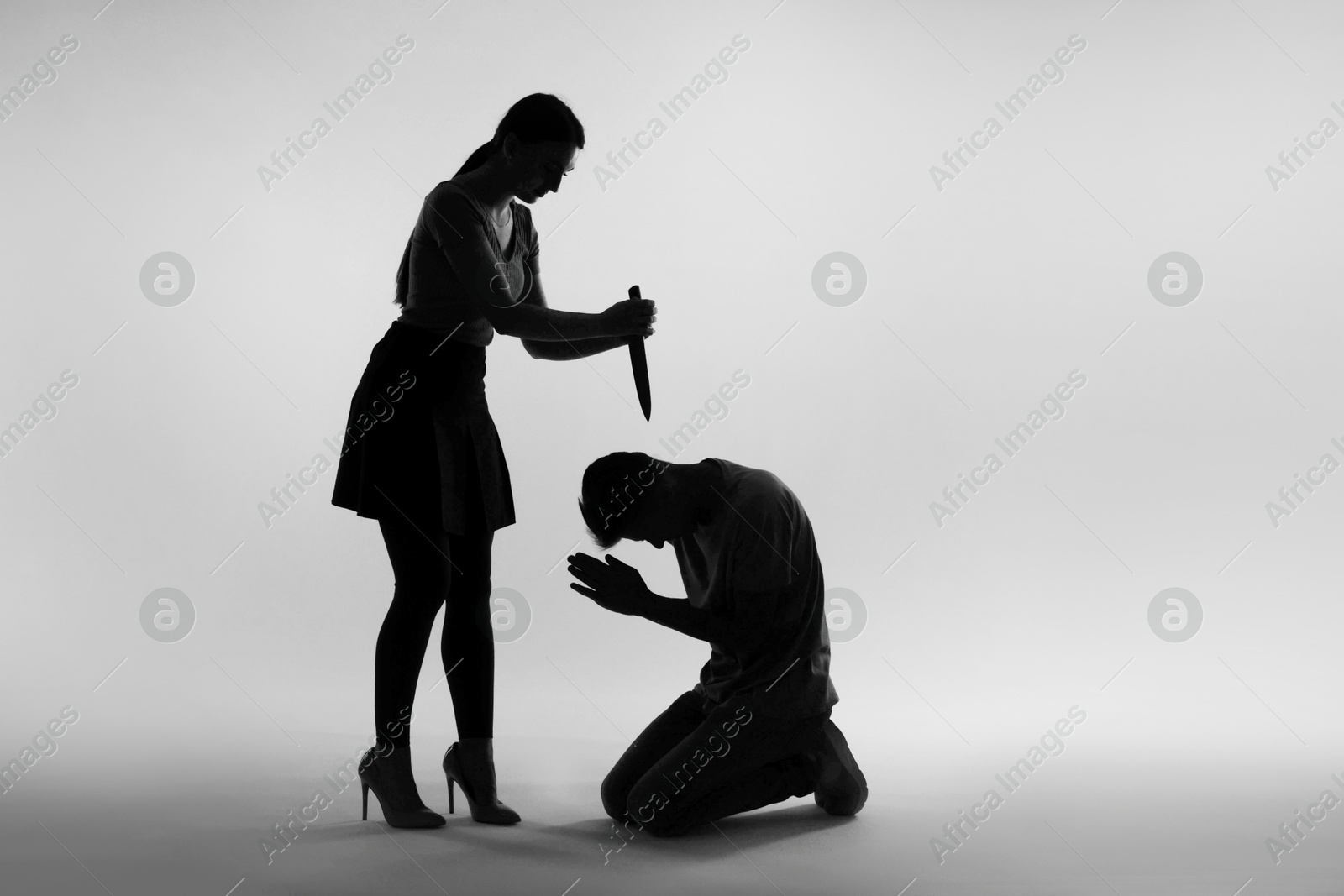 Photo of Domestic violence. Silhouette of woman with knife threatening her husband on grey background