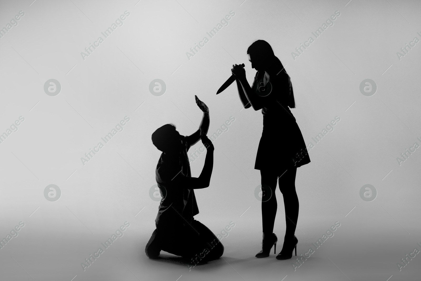 Photo of Domestic violence. Silhouette of woman with knife threatening her husband on grey background