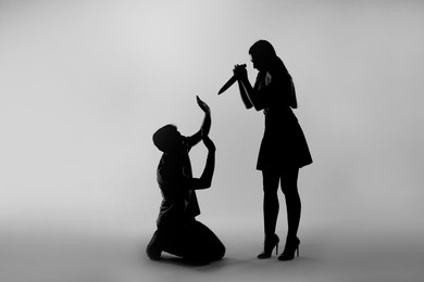 Domestic violence. Silhouette of woman with knife threatening her husband on grey background