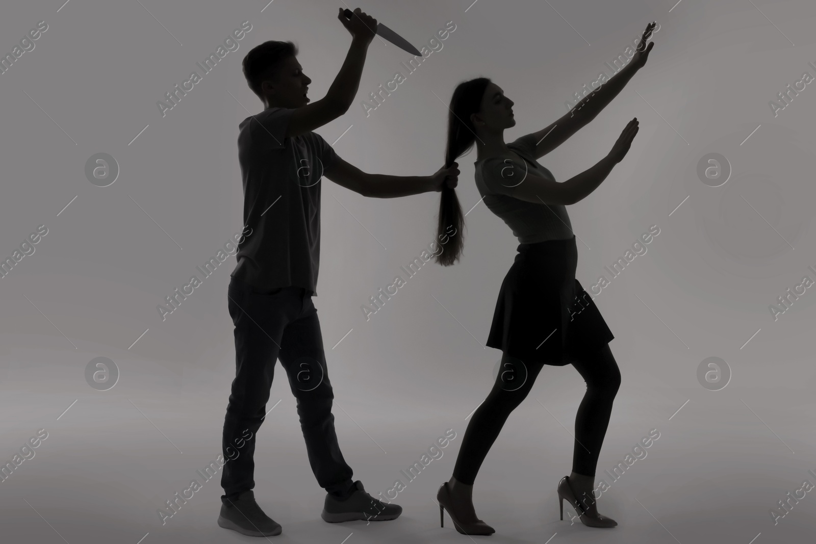 Photo of Domestic violence. Silhouette of man with knife trying to kill his wife on grey background