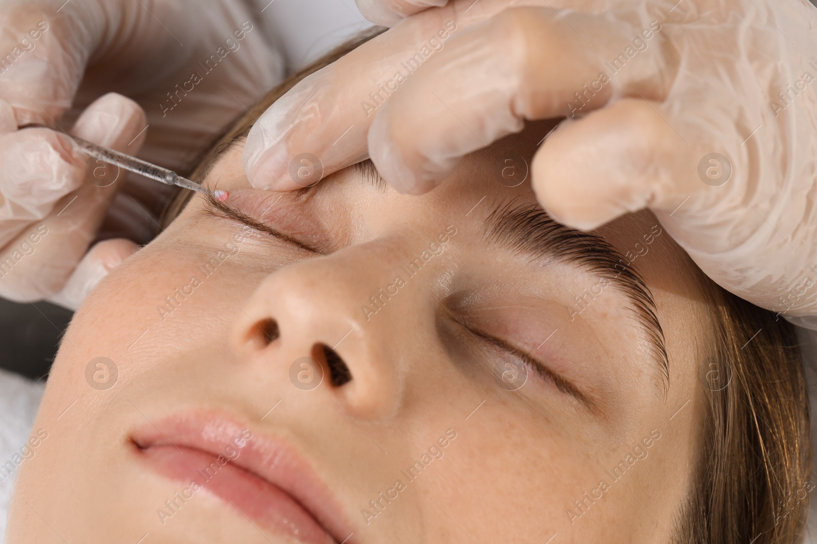 Photo of Eyelash lamination procedure. Esthetician applying adhesive on woman's eyelid in beauty salon, closeup